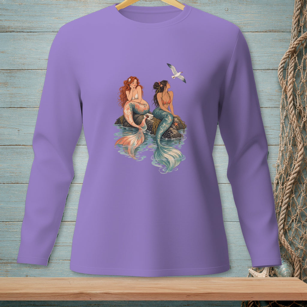 Two mermaids sit on rocks by the water with a seagull flying overhead.