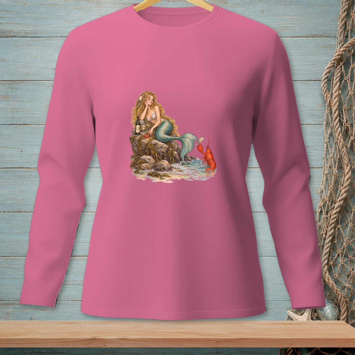 Mermaid sitting on rocks with wine and a lobster, displayed on pink long-sleeved shirt.