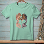 Mint t-shirt with a graphic of two mermaids applying makeup around a vanity.