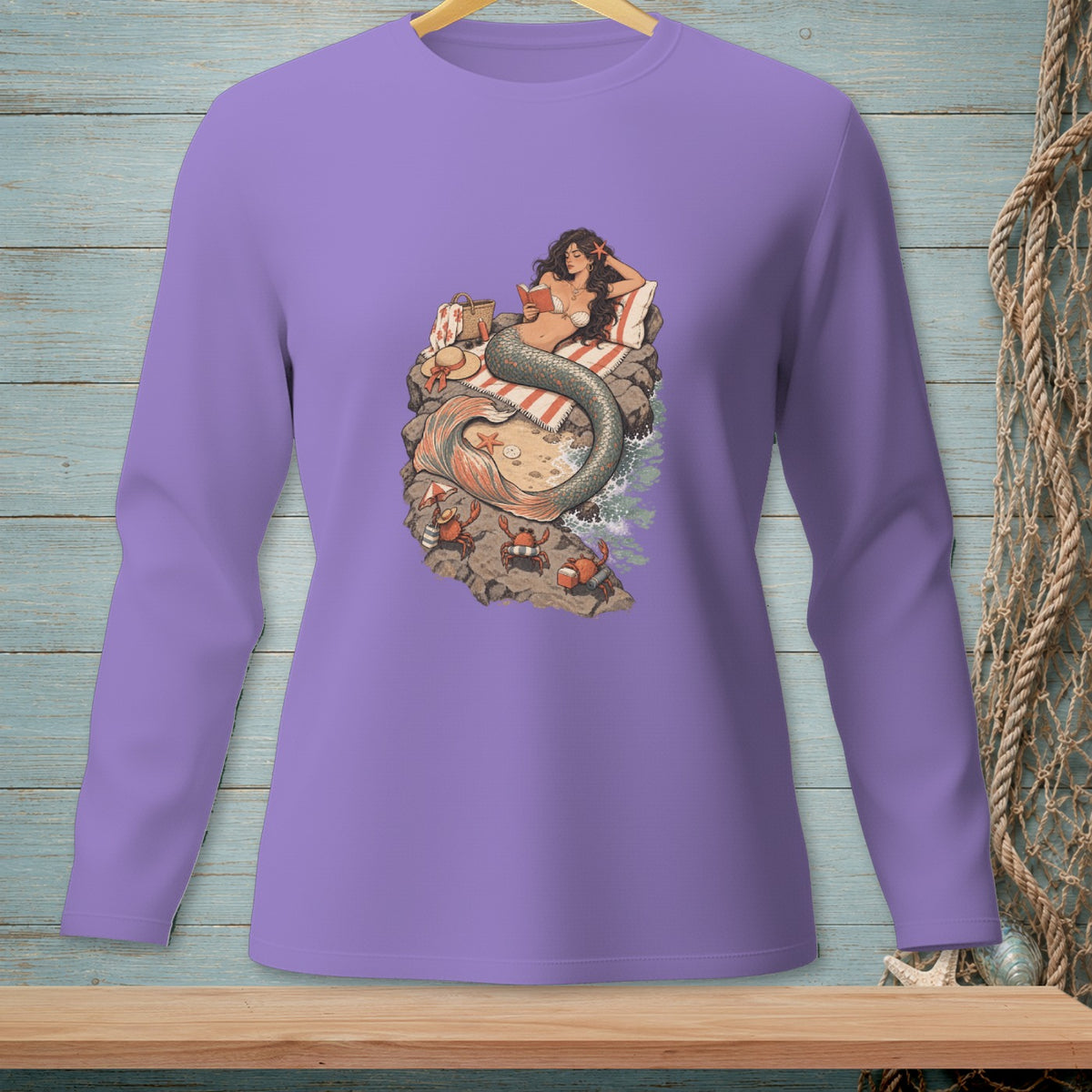 Mermaid reading on a beach with crabs, on a purple long-sleeve shirt.