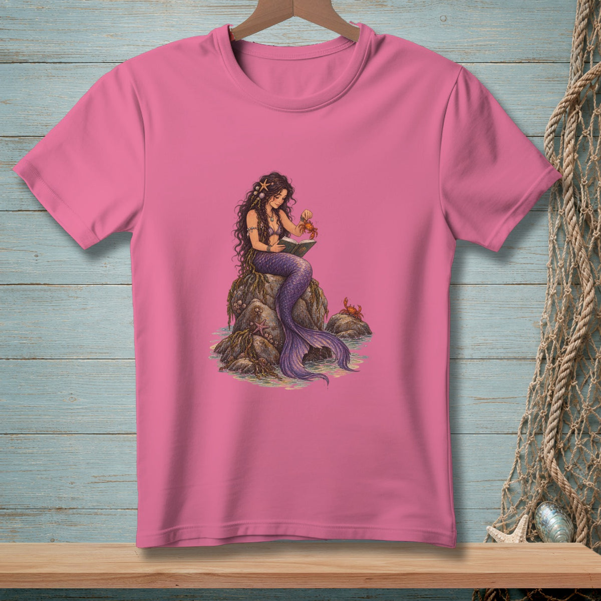 Pink t-shirt with illustration of a mermaid reading by the sea with crabs.