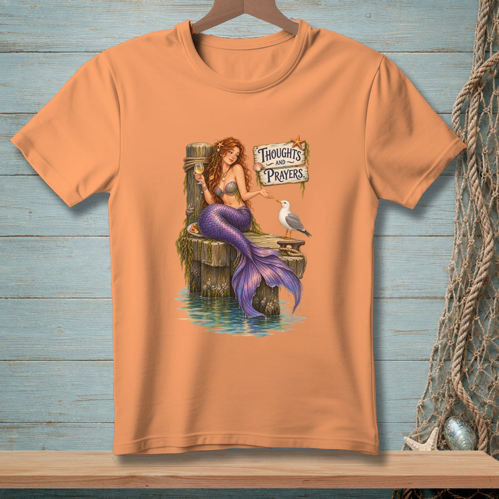 Mermaid with purple tail sitting on dock with a seagull and sign reading "Thoughts and Prayers".