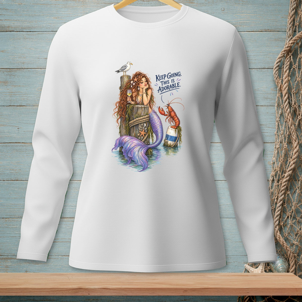 White long-sleeve shirt with a mermaid, lobster, and seagull graphic that reads "KEEP GOING. THIS IS ADORABLE."