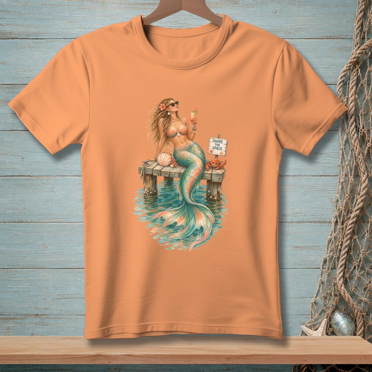 Orange t-shirt with a mermaid holding a drink on a dock with a crab and a sign that says "Share the Space".