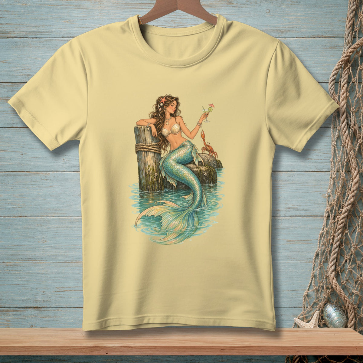 Yellow t-shirt with a mermaid sitting on a dock holding a drink and a crab.
