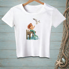 White t-shirt with a mermaid and seagull graphic on a wooden dock.