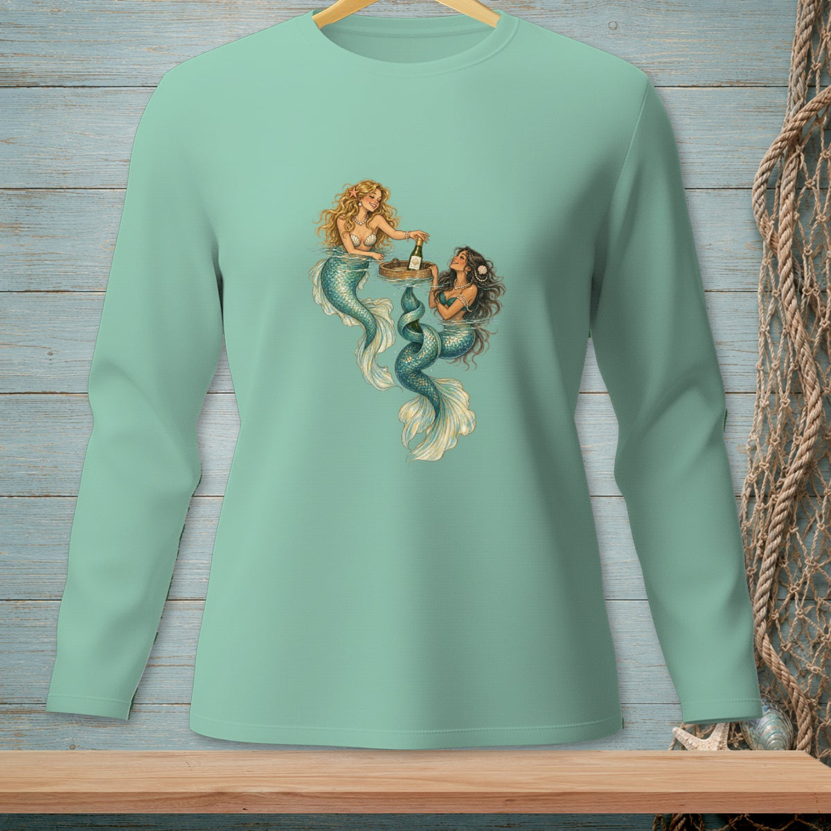 Two mermaids with teal tails share a drink on a wooden tray.