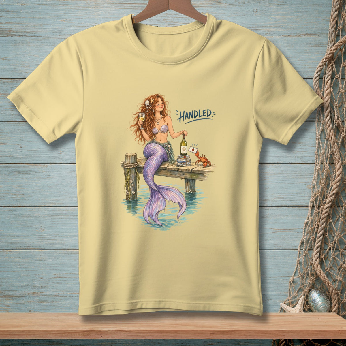 T-shirt with a mermaid holding wine and a crab on a dock, text "HANDLED".