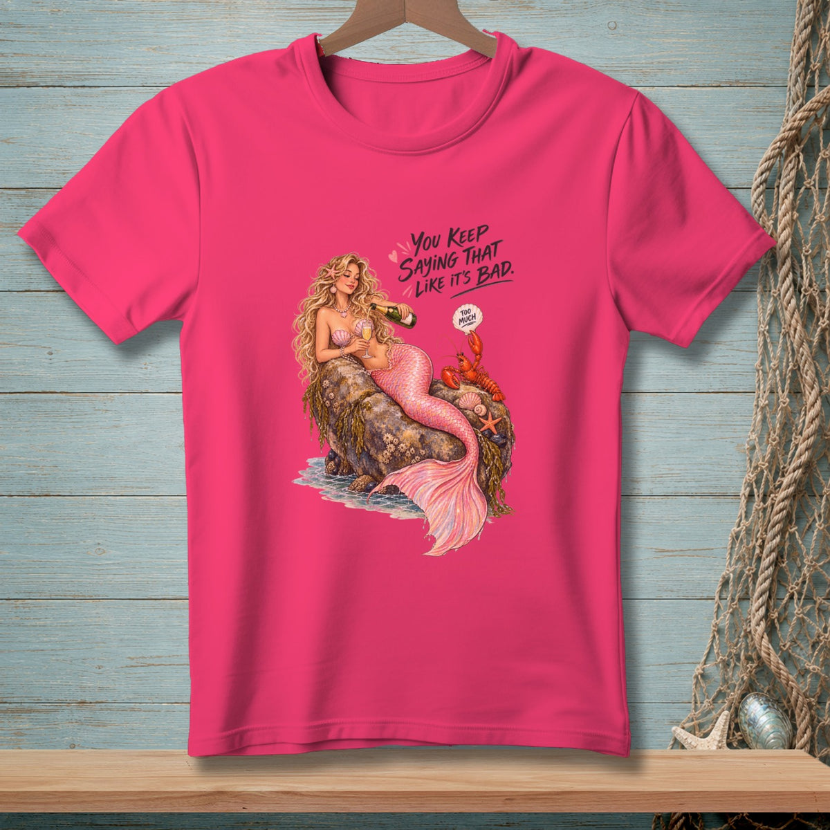 Pink t-shirt with mermaid, lobster, and text: "You keep saying that like it's bad. Too Much."