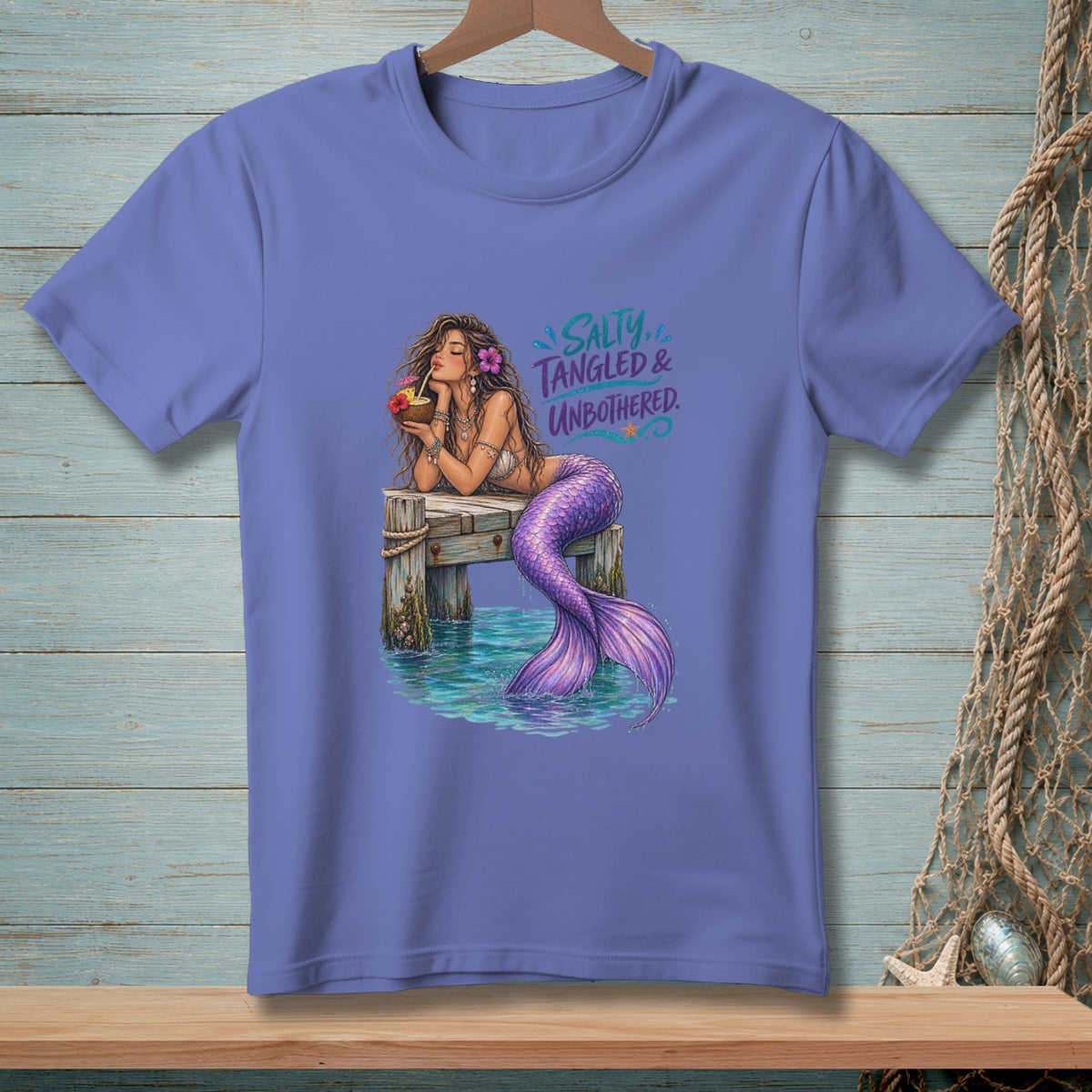 Mermaid drinking from coconut on pier with text "Salty, Tangled & Unbothered".