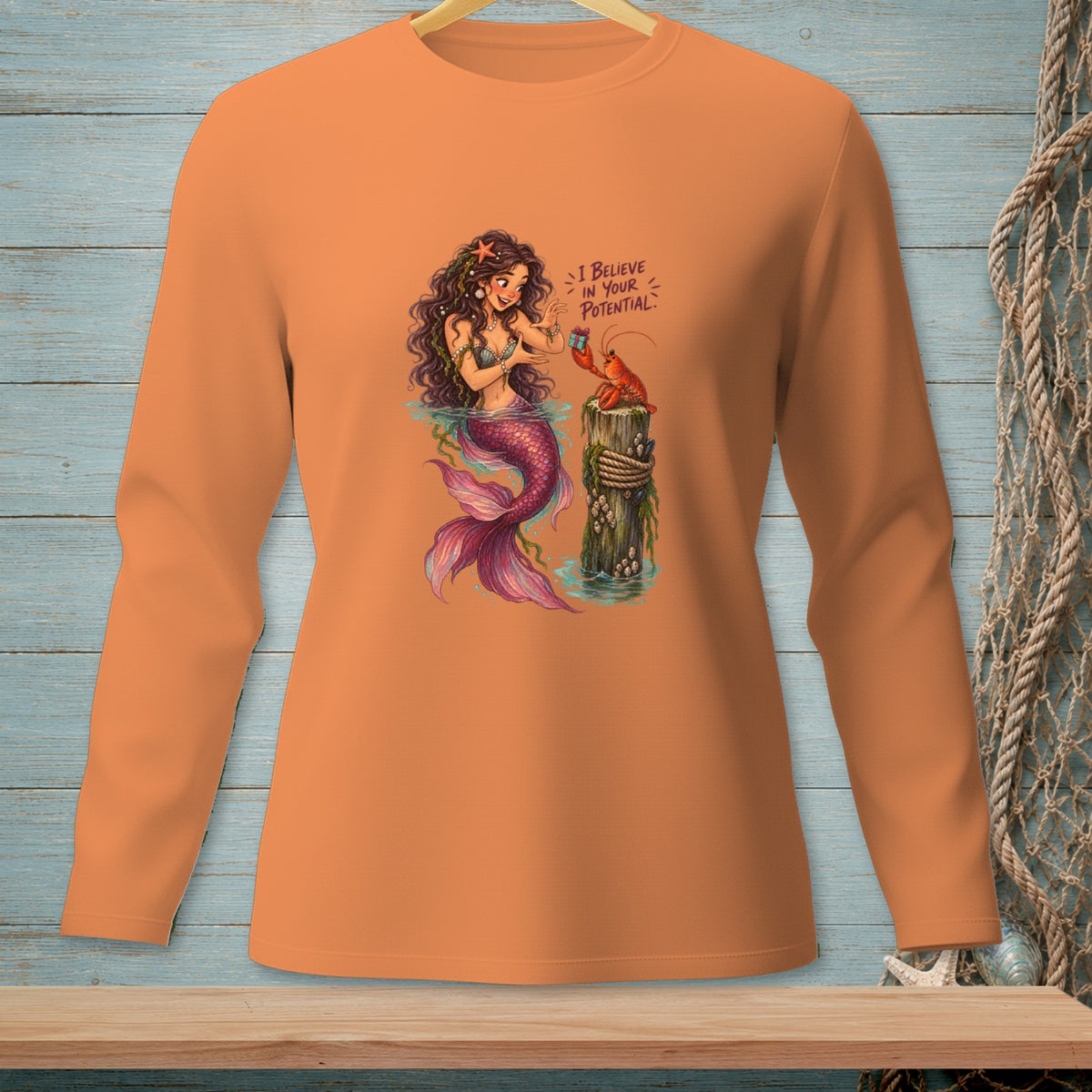 Orange long-sleeve shirt with a graphic of a mermaid and lobster, "I BELIEVE IN YOUR POTENTIAL."