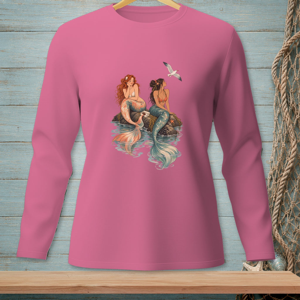Pink long sleeve shirt with a print of two mermaids sitting on rocks with a seagull flying above.