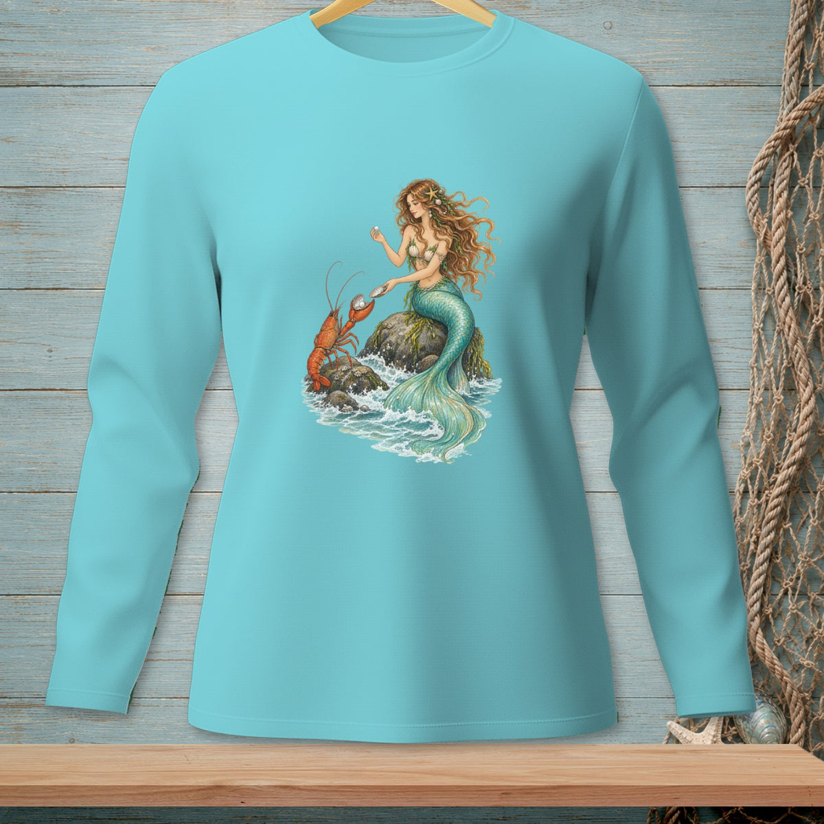 Long sleeve shirt with mermaid and lobster graphic on a rocky shore.