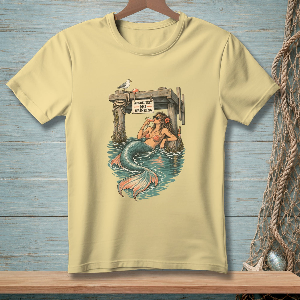 Light yellow t-shirt with graphic of mermaid drinking near "Absolutely No Drinking" sign.