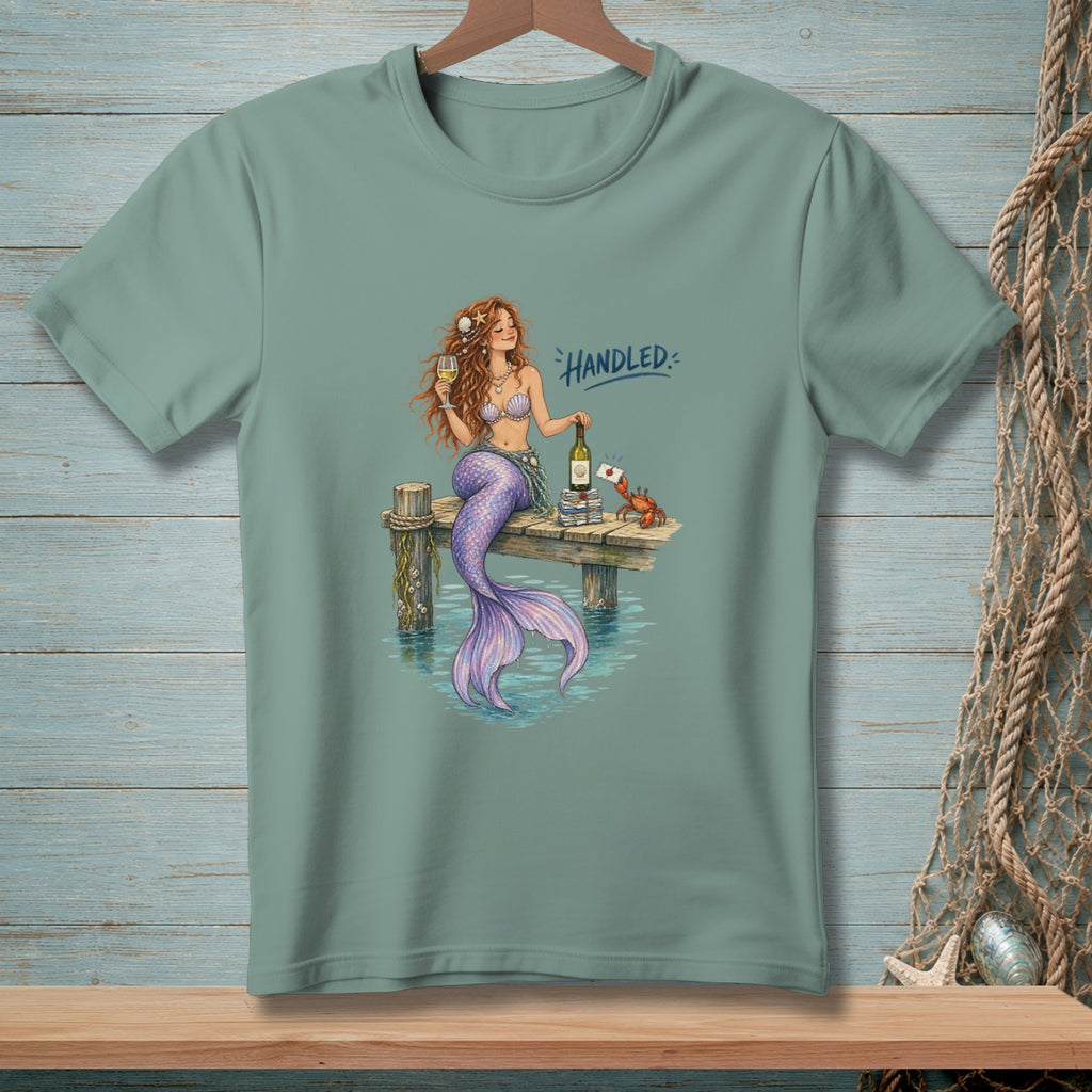 Mermaid with wine and books on a dock, text reads "Handled".