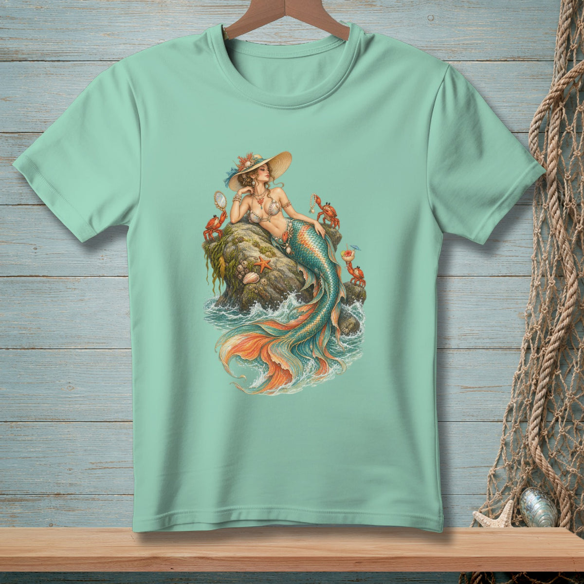 Mint green t-shirt with a detailed mermaid illustration sitting on a rock with crabs.