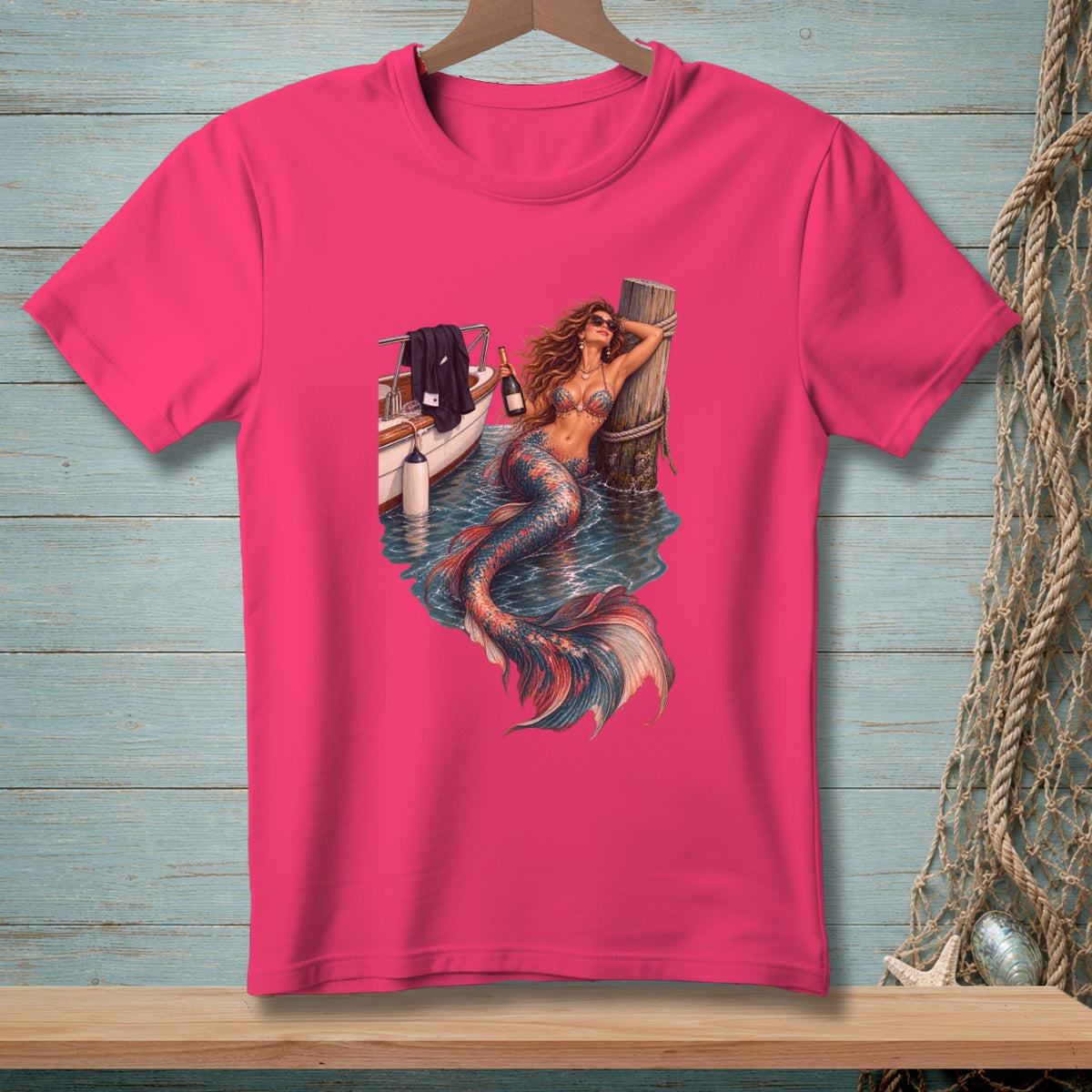 Pink t-shirt with a graphic of a mermaid by a boat holding a champagne bottle.