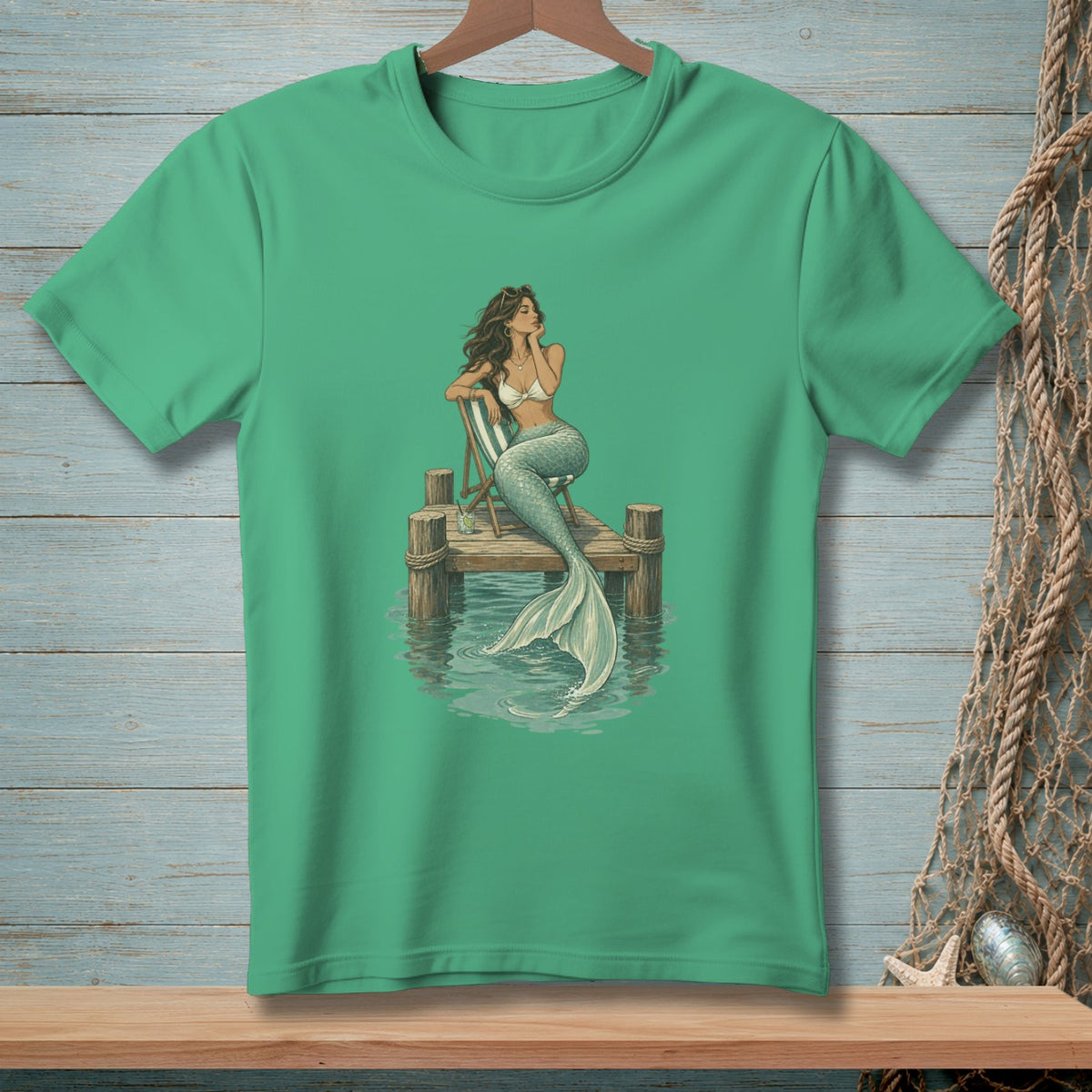 Green t-shirt with a printed graphic of a mermaid sitting on a dock.