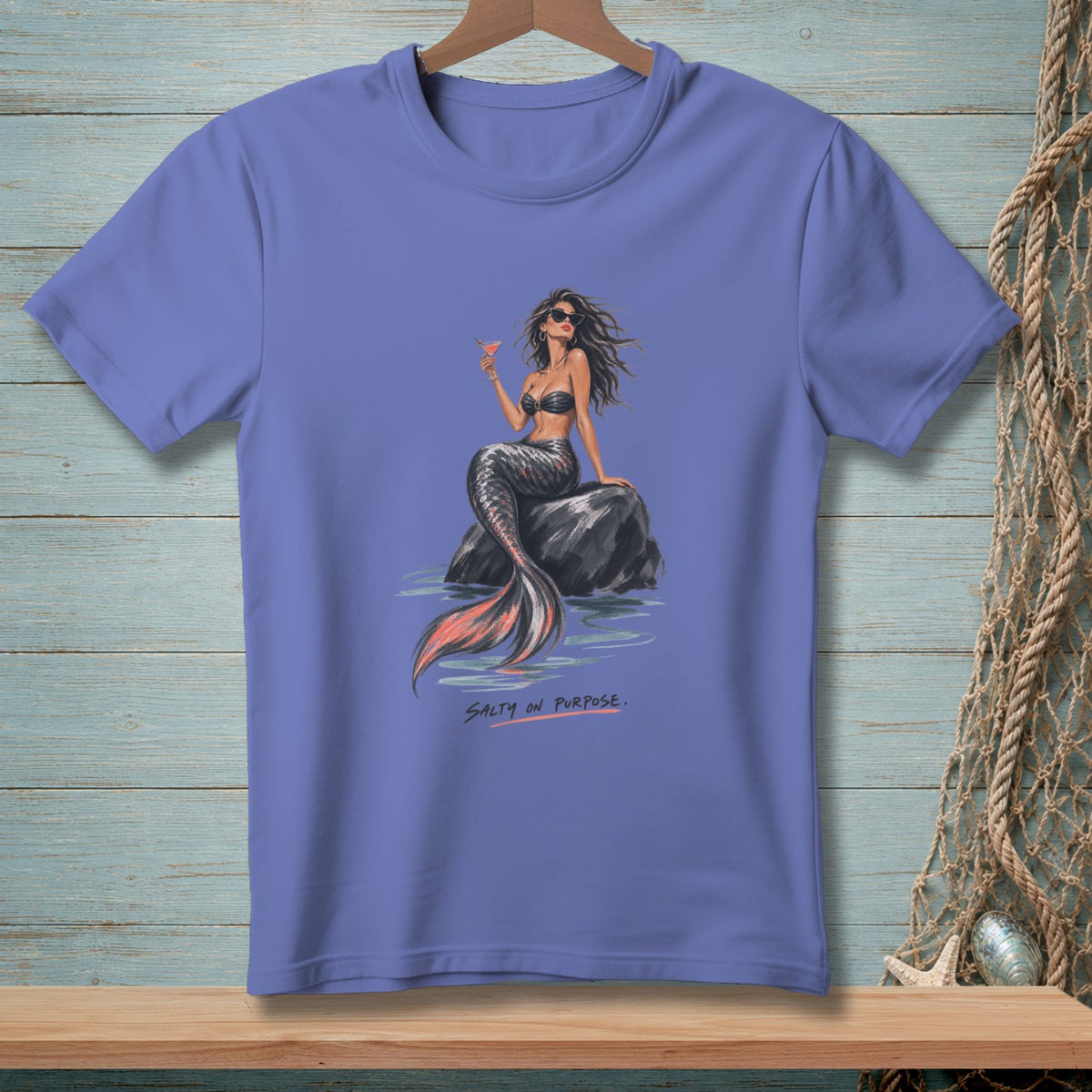 Purple t-shirt with illustration of a mermaid sitting on a rock holding a cocktail.