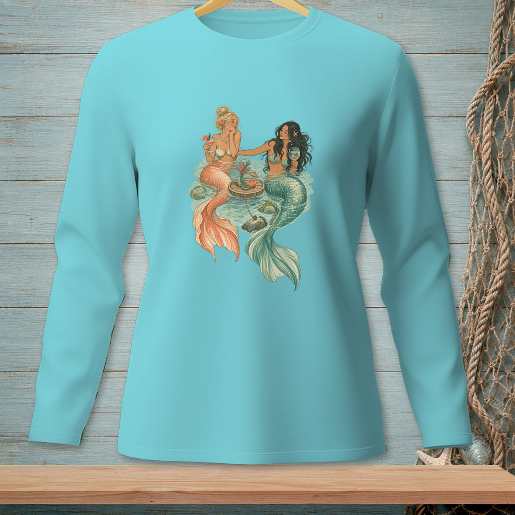 Two mermaids with tails, one blonde, one brunette, enjoying drinks by the sea.