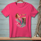 Pink t-shirt with a mermaid fishing off a wooden dock.