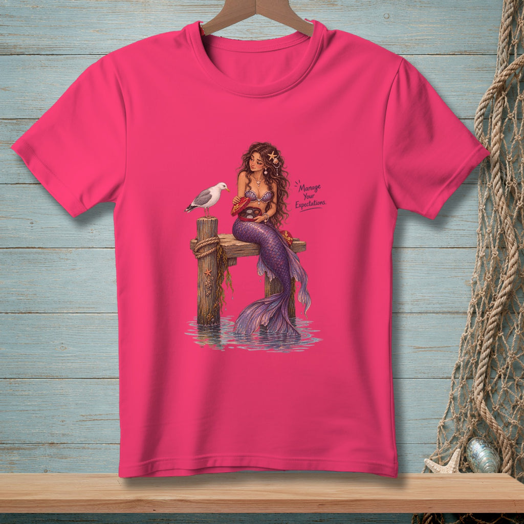 Mermaid on pier with seagull and box of chocolates, text "Manage Your Expectations."