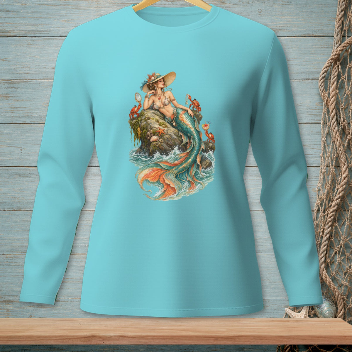 Long-sleeve teal shirt with mermaid graphic on rock, crabs, and sea.
