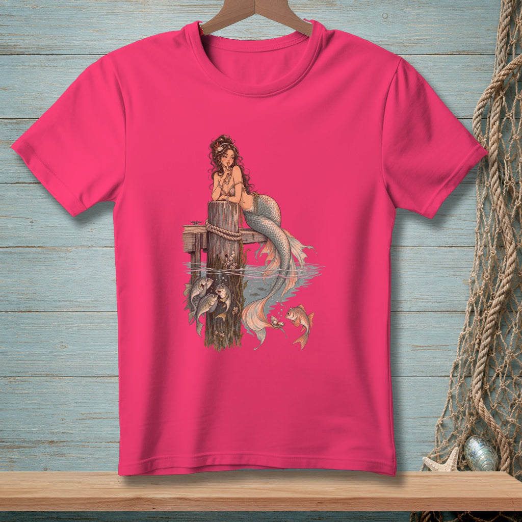 Pink t-shirt with illustration of a mermaid and fish by a wooden post.