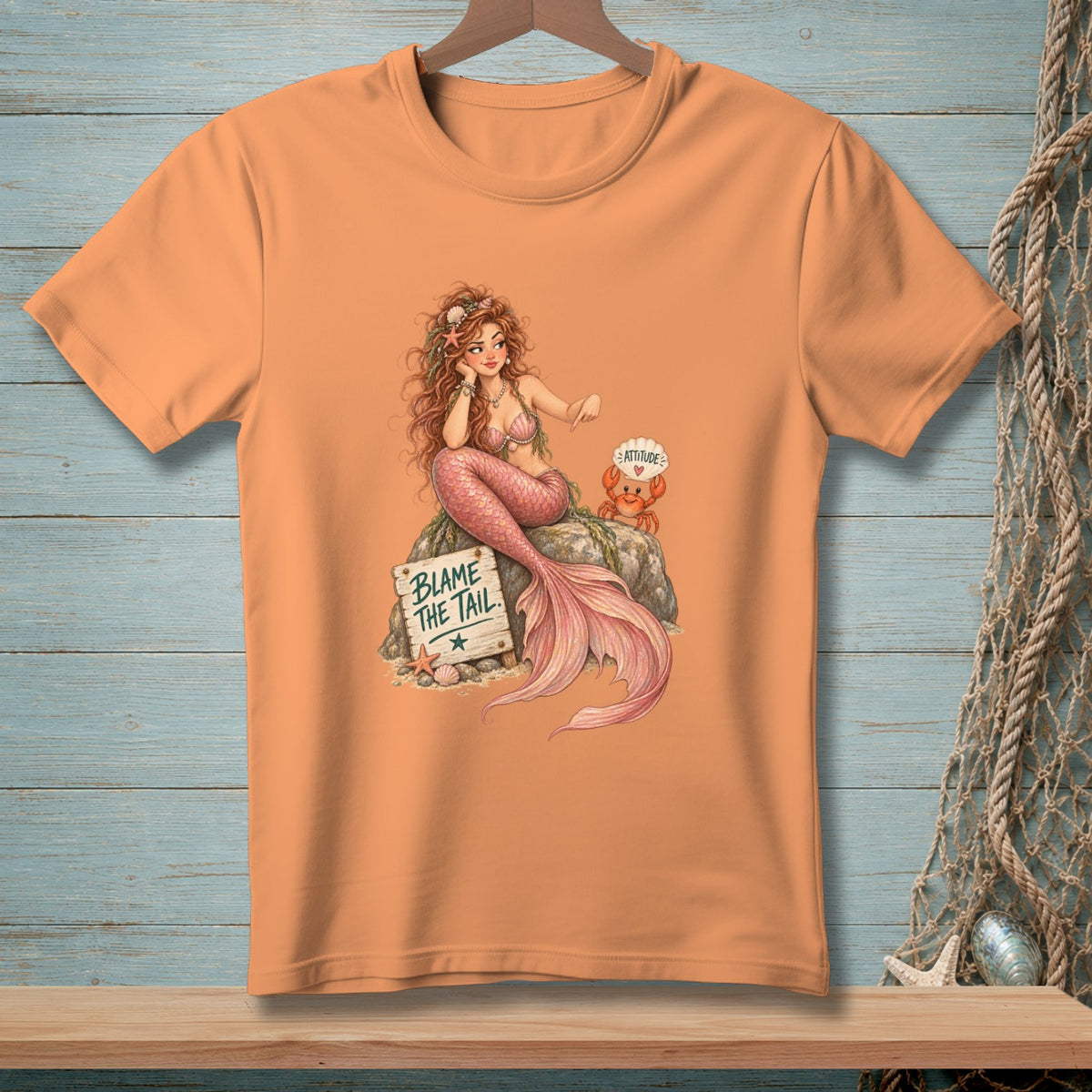 Peach t-shirt with mermaid, crab, and "Blame The Tail" sign.