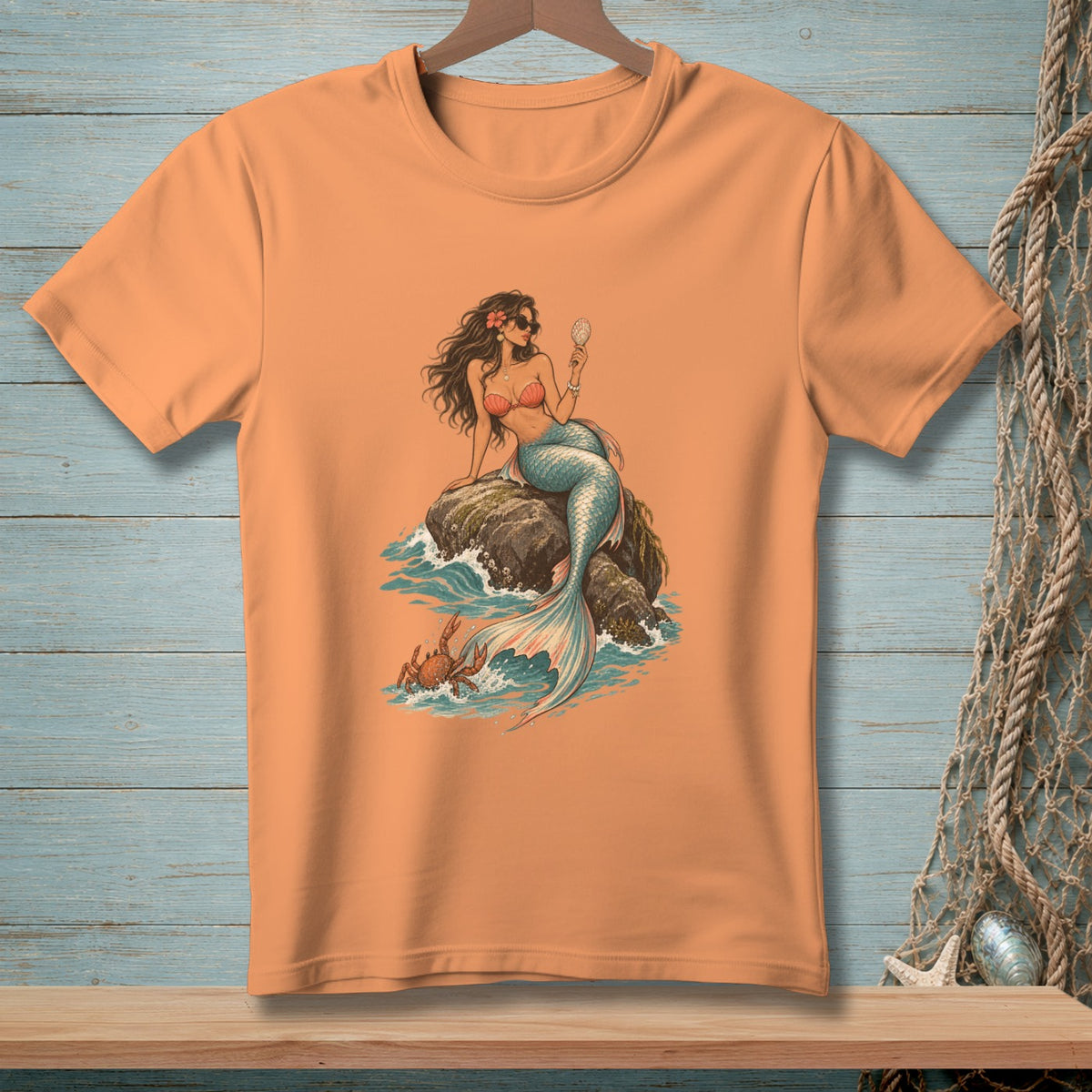 Orange t-shirt with a graphic of a mermaid holding a shell and a crab by the water.