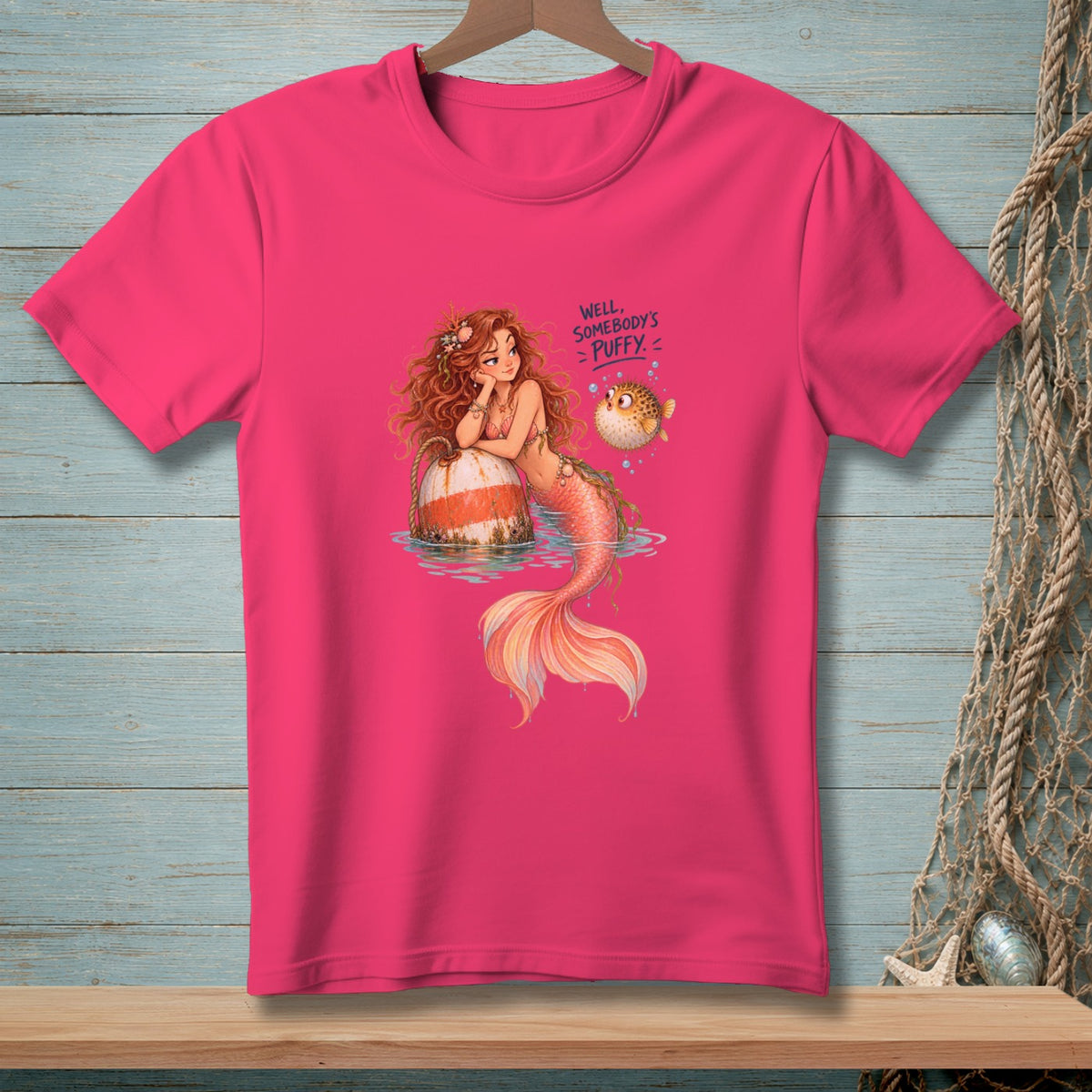 Pink t-shirt with mermaid leaning on a buoy and a pufferfish with text "Well, Somebody's Puffy".
