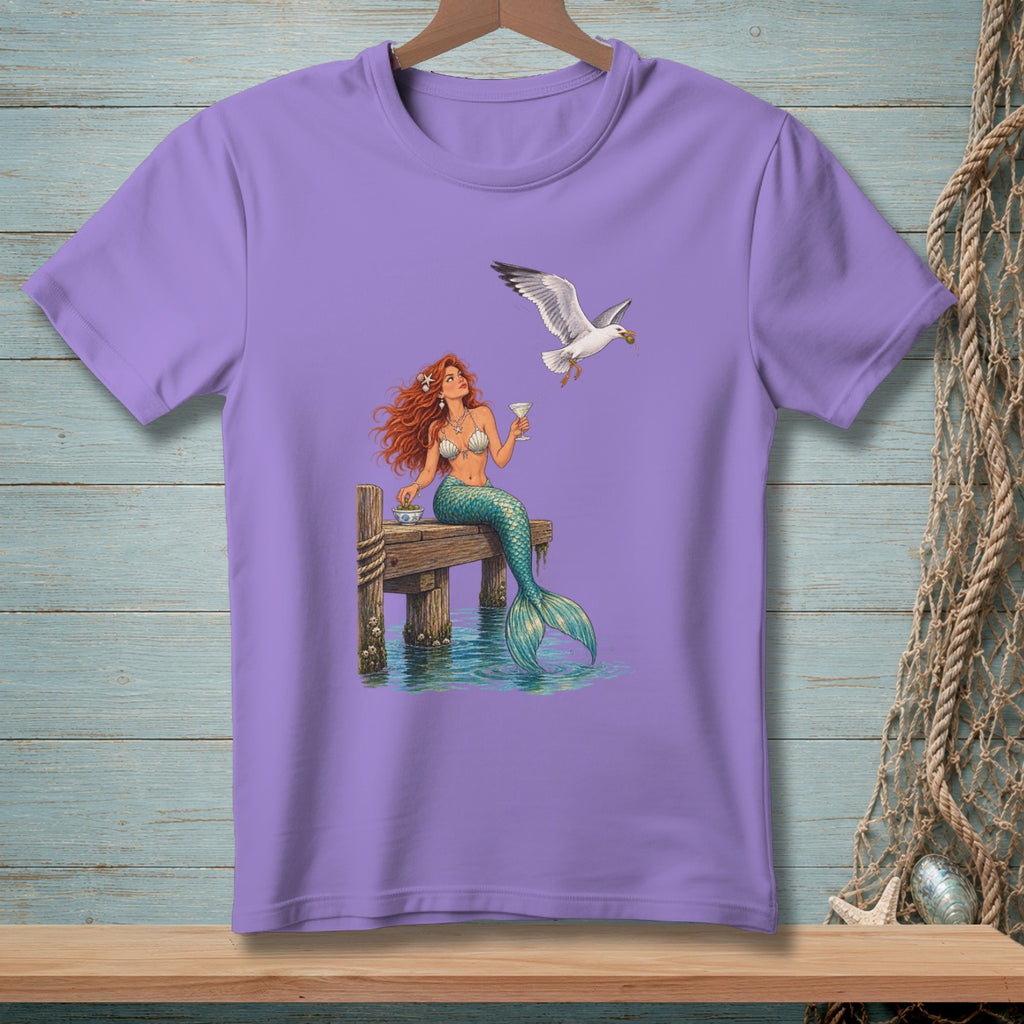 Lavender t-shirt with a mermaid holding a drink near a seagull on a dock.