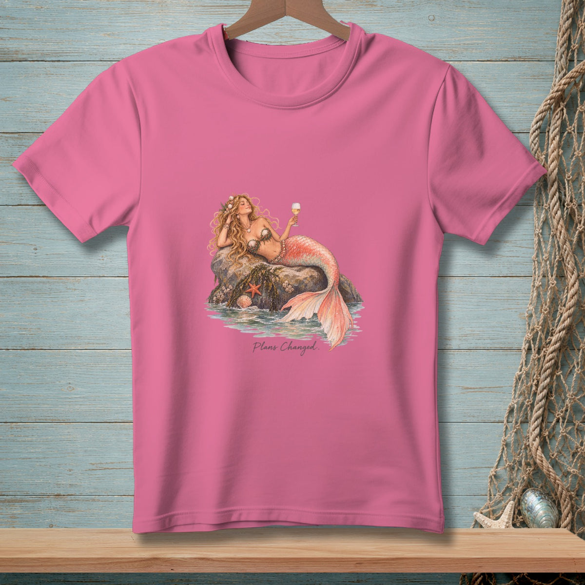 Pink t-shirt featuring an illustration of a mermaid lounging on a rock, holding a glass, with the text "Plans Changed."