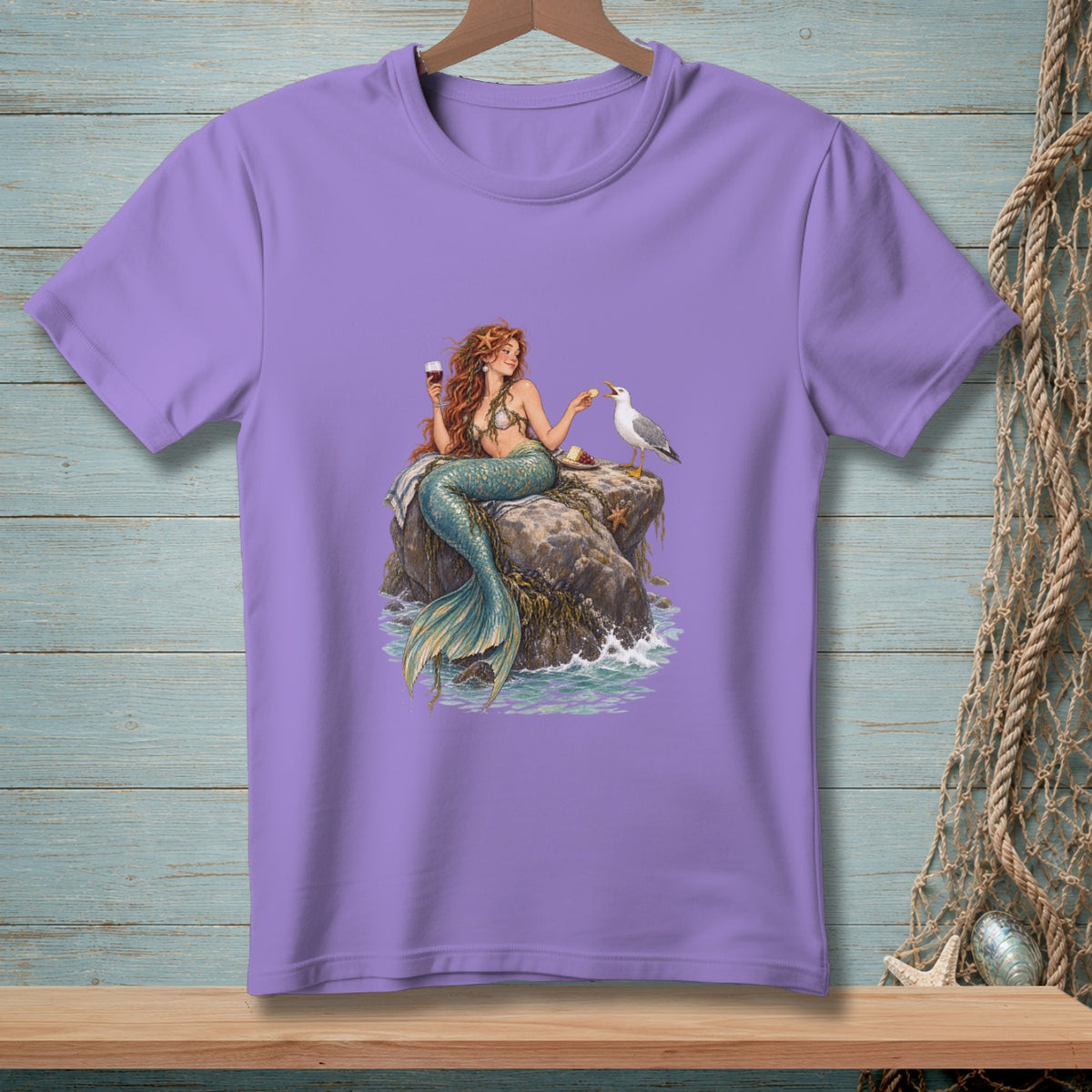 Purple t-shirt with mermaid holding wine, feeding a seagull on a rock.